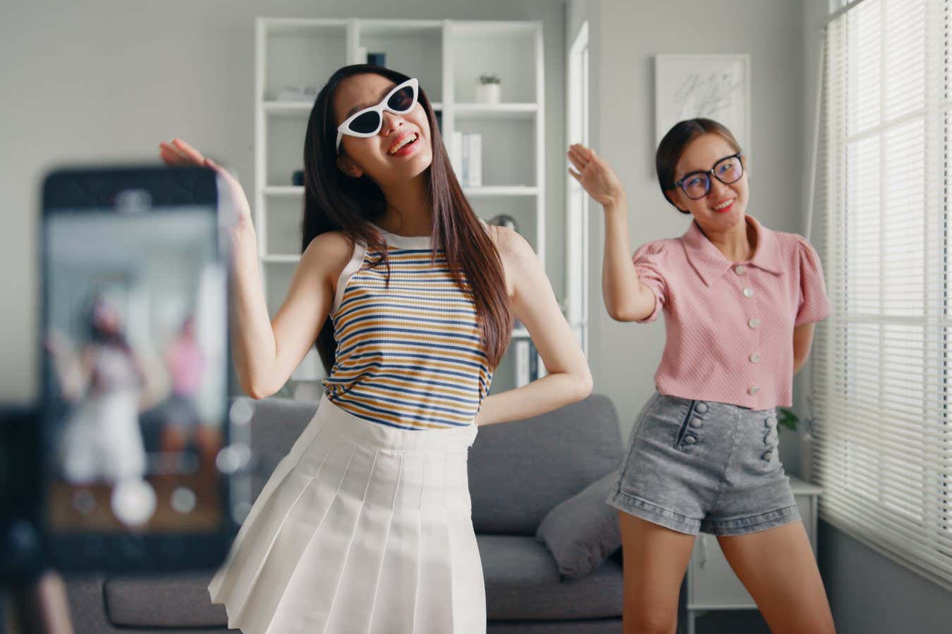 Asian young woman with her friend tiktoker created her dancing video by smartphone camera together. To share video on social media application; Shutterstock ID 2159904237; purchase_order: -; job: -; client: -; other: -